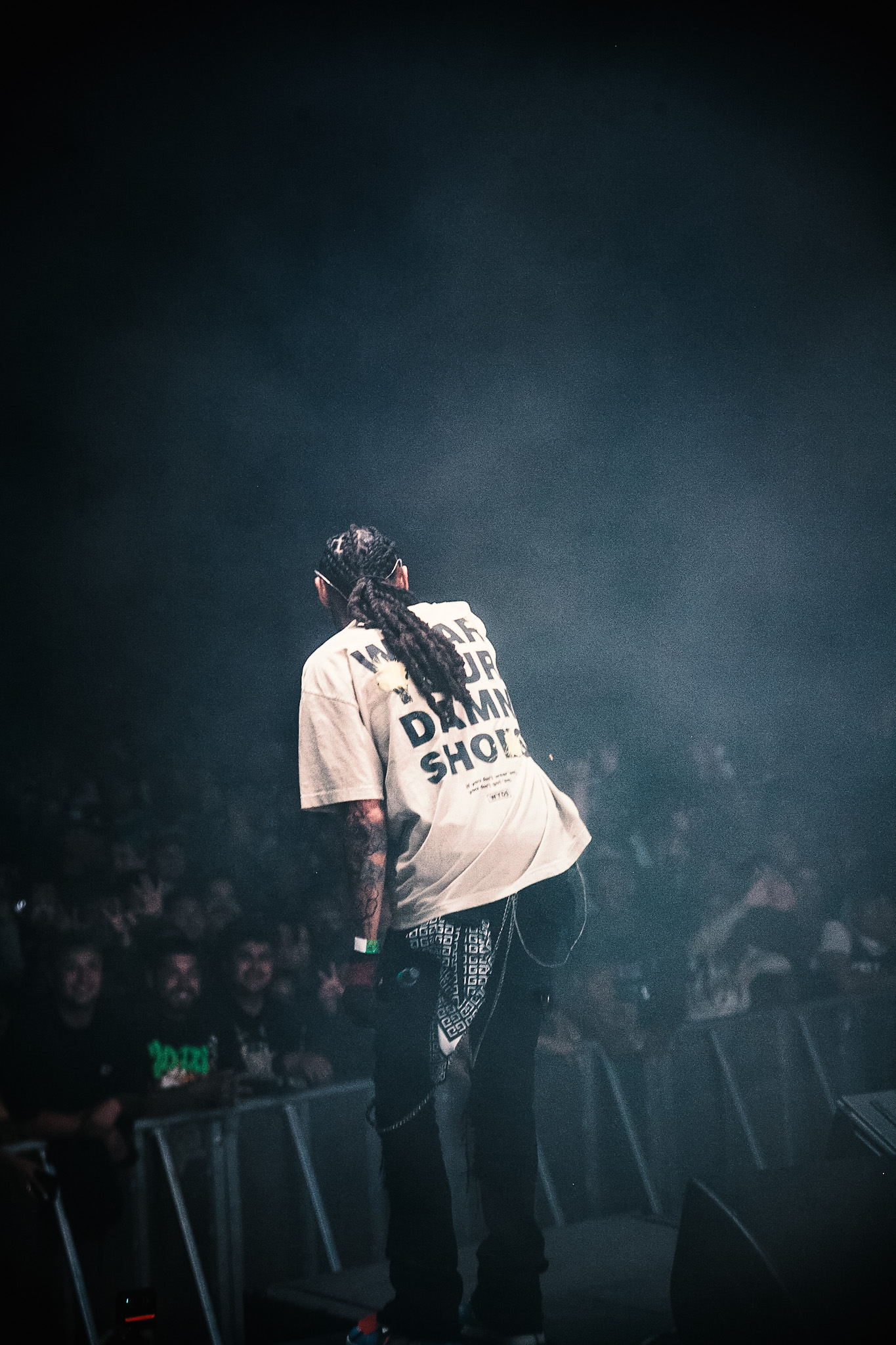 Kilohana seen from behind performing for a crowd in dark, hazy stage lighting