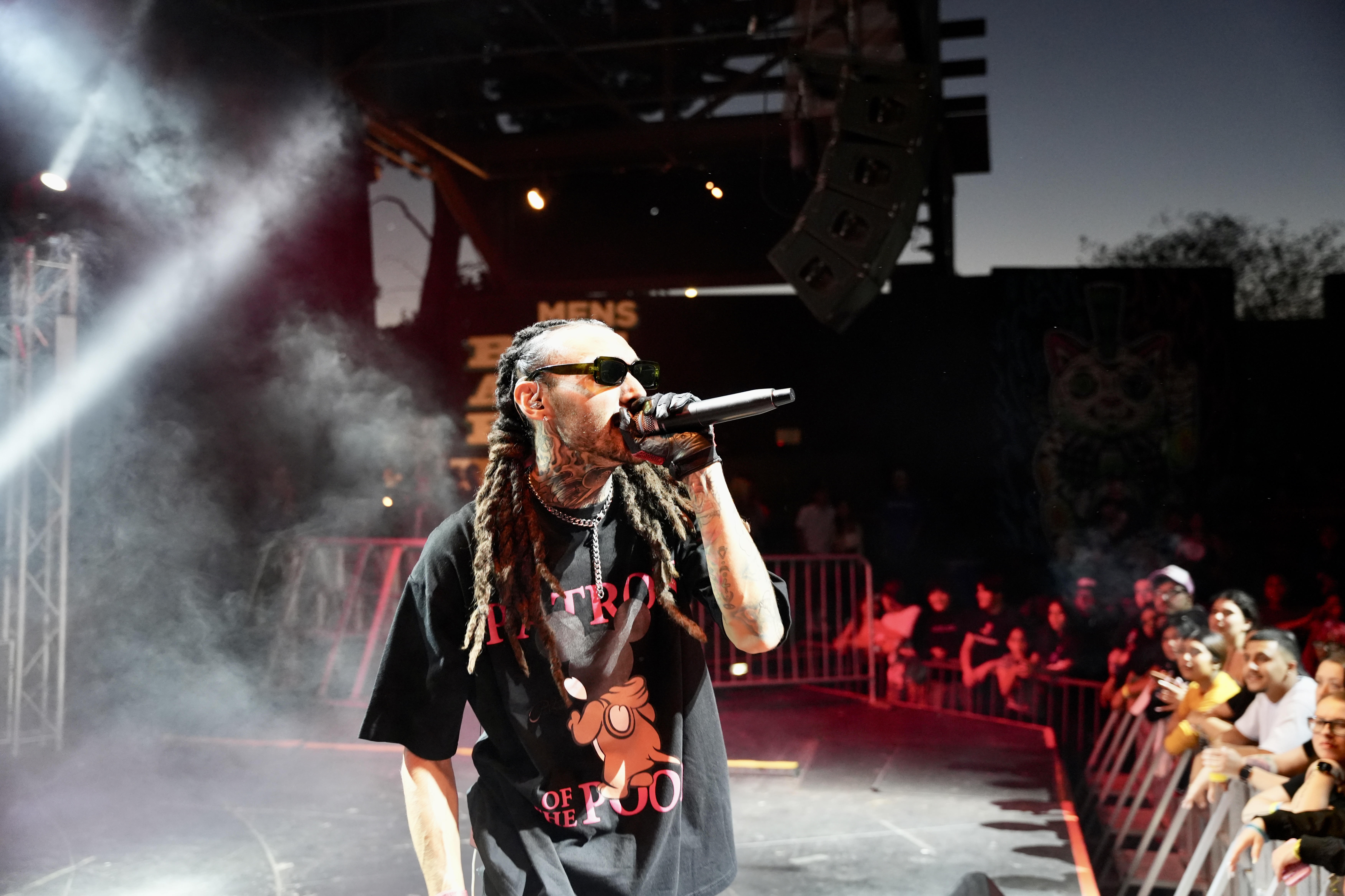 Kilohana singing into a microphone on stage with the crowd visible beside him