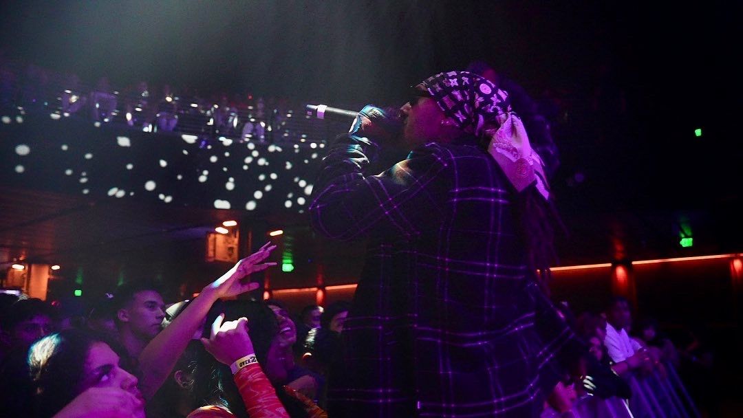 KILOHANA in a plaid jacket performing as fans reach toward him in the purple-lit pit at Novo